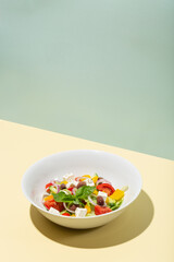 Greek salad in white plate hard shadows on blue and yellow