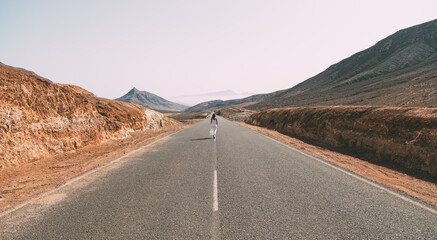 Unrecognizable woman walking on road near hills under cloudy sky