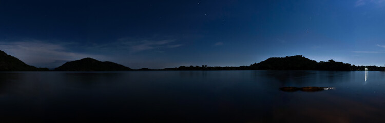 Panoramic shot of sea view with mountains in the background under a cloudy sky at night © Kitraveler/Wirestock