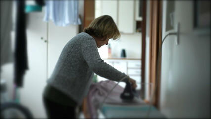 Casual senior woman doing housework chores at laundry room