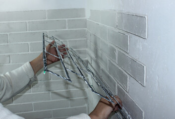 Close-up - a woman's hand removes the stencil from the decorative plaster on the wall. House...