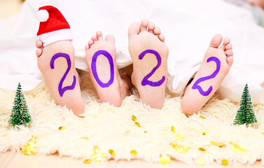 2022, numbers and date of 2022 on children's legs painted with purple paints, the color of the year is purple, children's creativity, signs and numbers, body art.
