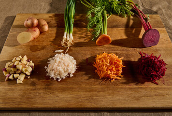 Close-up of seasonal fresh raw vegetables on a wooden board, cut in half and the other half shredded on a grater. Beets, carrots, green onions with leaves and potatoes. Food background