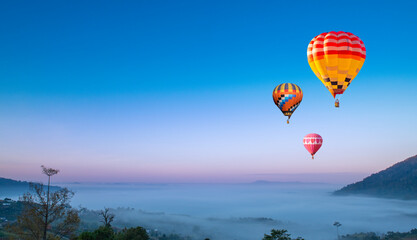 Beautiful hot air balloons flying above foggy landscape in morning ,green mountain in nature with blue sky background.