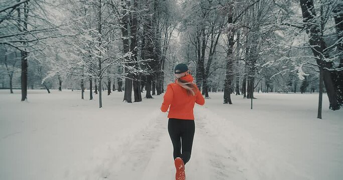 Running woman, girl runner on snow in park in winter sunny day. Female in pink sportswear jacket fitness training outdoors. Run, Sport concept, leisure and freedom.
