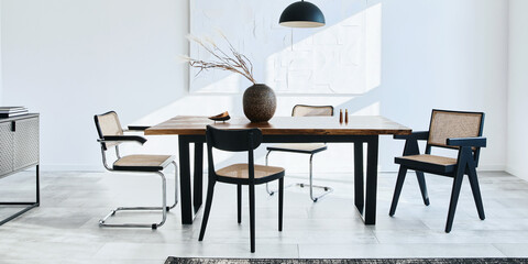Minimalist composition of dining room interior with wooden table, design chairs, dried flowers in a vase, black pendant lamp, art paintings on the wall and elegant personal accessories. Template.