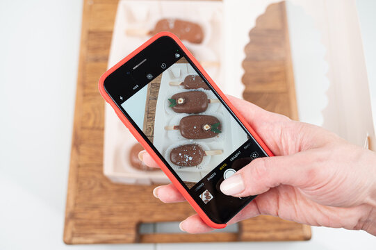  Woman makes a photo of cupcakes on a smartphone ice cream popsicle cake, close up