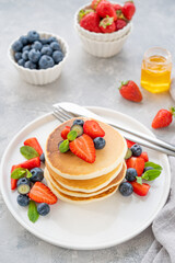 A stack of delicious fluffy pancakes with berries and honey on a white plate on a gray concrete background. Copy space.