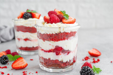 Red Velvet cake trifle with fresh berries in a glass jar on a gray concrete background. Dessert for Valentine's Day. Copy space.