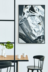 Stylish open space interior with wooden family table, black chairs, cups of coffee, tropical leaf in vase, abstract painitings on the wall and elegant accessories. Modern home decor. Template.