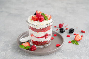 Red Velvet cake trifle with fresh berries in a glass jar on a gray concrete background. Dessert for Valentine's Day. Copy space.