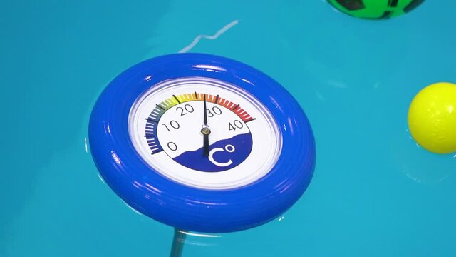 Blue thermometer and swimming balls floating in water in pool. Close up view.