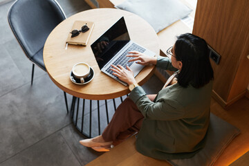Fototapeta na wymiar High angle portrait of young Asian woman using laptop in cafe while working remotely, copy space
