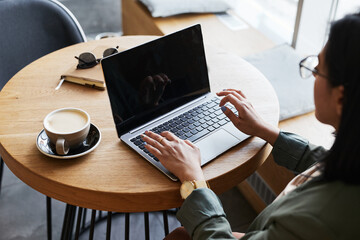 Close up of young Asian woman using laptop in cafe while working remotely in elegant wooden...