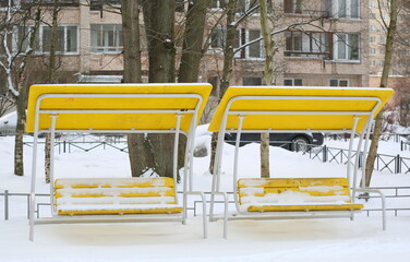 Two yellow wooden swing benches with plastic canopies in the courtyard of a residential building