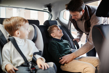 Portrait of man buckling son in back seat of family car, copy space
