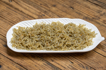 The dried clove fish in the container is on the wood grain table