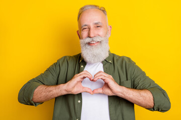 Photo portrait of senior man laughing showing heart shaped sign with hands isolated vibrant yellow color background