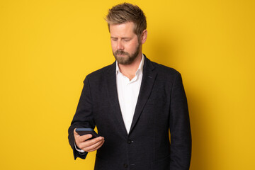 Young business man using smartphone standing over yellow background.