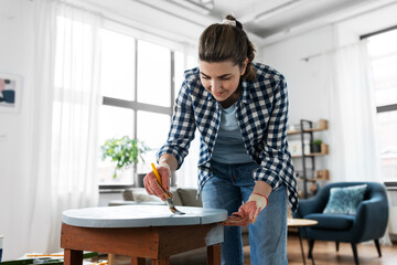 renovation, diy and home improvement concept - woman in gloves with paint brush painting old wooden table to grey color