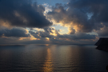 A thundercloud in the orange-yellow light of sunset. Dramatic stormy sky. Huge cumulus clouds over the ocean. A harbinger of bad weather, climate change, natural disaster. Light and shadow reflections