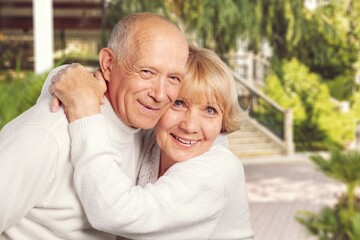 Senior couple spending time in sunny garden together embracing and smiling.