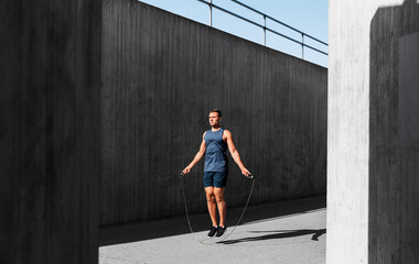 fitness, sport and exercising concept - man skipping with jump rope outdoors