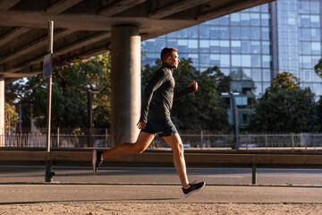 Obraz na płótnie Canvas fitness, sport and healthy lifestyle concept - young man running outdoors under bridge