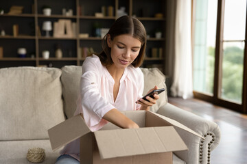 Young woman, shopper, consumer receiving parcel, unboxing package from internet store, producing...