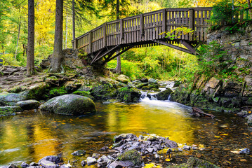 Wooden bridge over the Oker river with large stones on Engagement island in the Harz Mountains, - obrazy, fototapety, plakaty