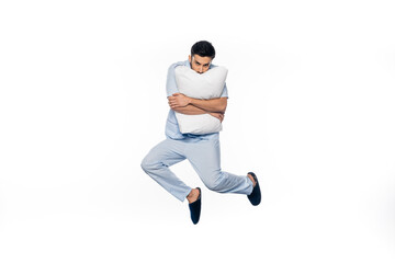 young man in pajamas levitating and hugging pillow isolated on white.