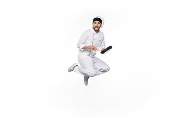 Fototapeta na wymiar cheerful chef in hat and uniform jumping and holding frying pan with wooden spatula isolated on white.