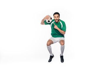 amazed football player in uniform jumping while pointing at soccer ball isolated on white.