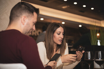 a wedding couple use their cell phone while waiting for food in a restaurant.Valentine's Day.
