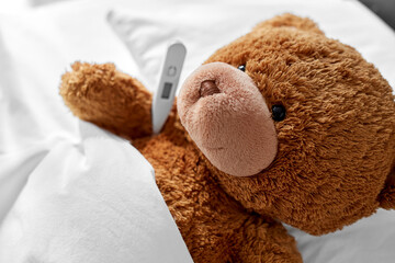 medicine, healthcare and childhood concept - ill teddy bear toy head with thermometer lying in bed