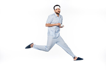 bearded man in pajamas holding cup and saucer while levitating on white.