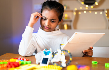 Thoughtful Young girl kid preparing DIY robot by seeing instruction manual at home - concept of making scientific experiment, Childhood learning, education and prodigy.