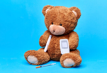 medicine, healthcare and diabetes concept - teddy bear toy with syringe, glucometer and insulin pen device over blue background