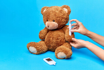 medicine, healthcare and diabetes concept - hands with insulin pen making injection to teddy bear toy over blue background