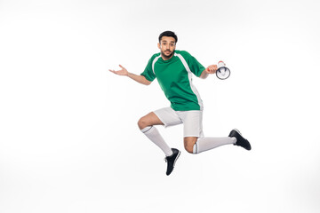 Fototapeta na wymiar confused football player in uniform jumping and holding loudspeaker on white.