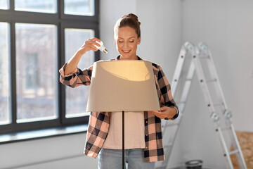 moving, electricity and repair concept - woman changing light bulb in floor lamp at new home