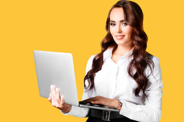 This is portrait of beautiful Caucasian girl of 30 years old with laptop in her hands on yellow background. Young woman holds open laptop in her hands and looks at camera and smiles with snow-white