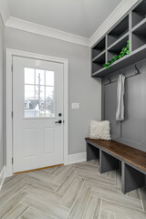 A staged, gray mudroom / entryway with bench seating, coat hooks, and storage above. A scarf hangs...
