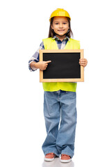 building, construction and profession concept - smiling little girl in protective helmet and safety vest holding chalkboard over white background