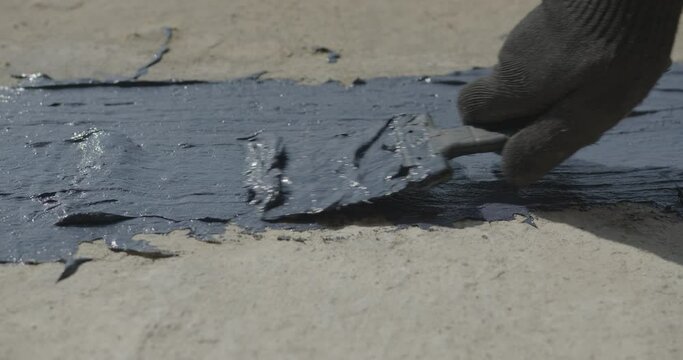 a hand in a mitten applies a brush of blue paint to a concrete floor at a construction site. applying epoxy paint to biton. Blue putty on concrete. close-up