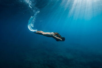 Fototapeta na wymiar Freediver woman in bikini with fins dive underwater in deep blue sea.