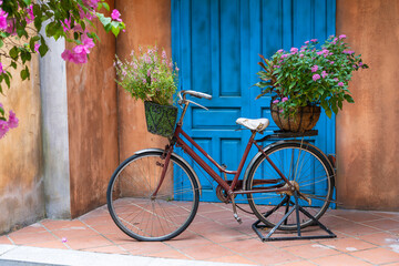 Fototapeta na wymiar Vintage bike with basket full of flowers next to an old building in Danang, Vietnam, close up