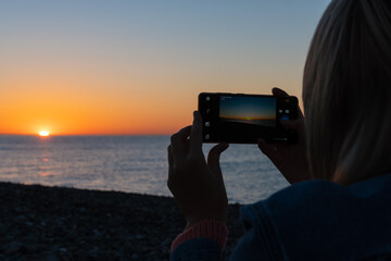 Close-up of women's hands with a mobile phone that horizontally photograph a beautiful sunset on the sea, copy space