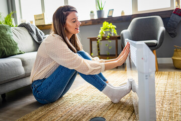 Young Woman With sweater Suffering From Cold Sitting Near Heating Radiator At Home. Energy Saving...