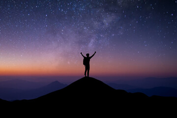 Young traveler with backpack standing and open both arm watched night sky view, star and milky way alone on top of the mountain. He enjoyed traveling and was successful when he reached the summit.